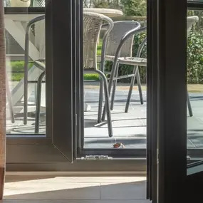 Geöffnete Terrassentür mit Blick auf Gartenmöbel und sonnige Terrasse im Grünen.