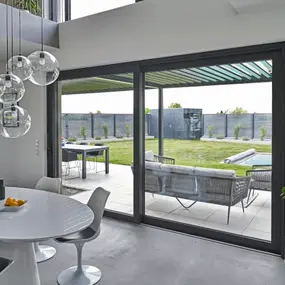 Modernes Wohnzimmer mit großen Glas-Schiebetüren, Blick auf Terrasse und Garten mit Pool.